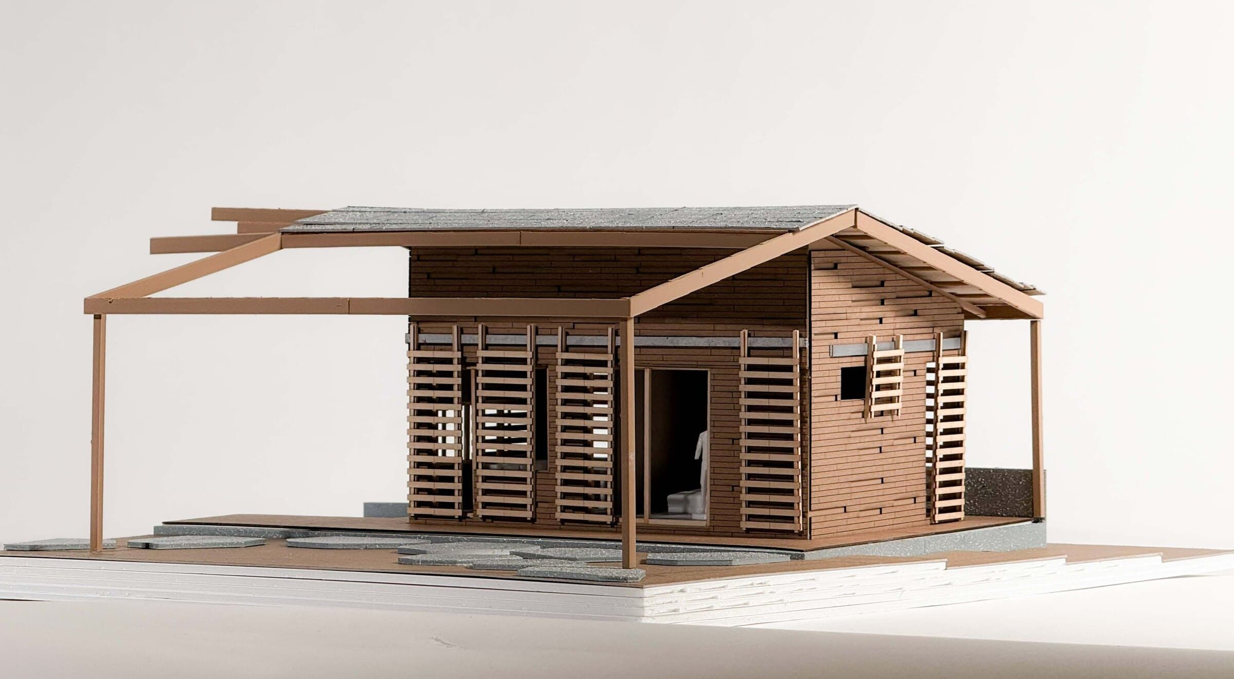 Physical model photograph of a Príncipe Eco-Village housing unit with timber slat screens and a deep overhanging roof.