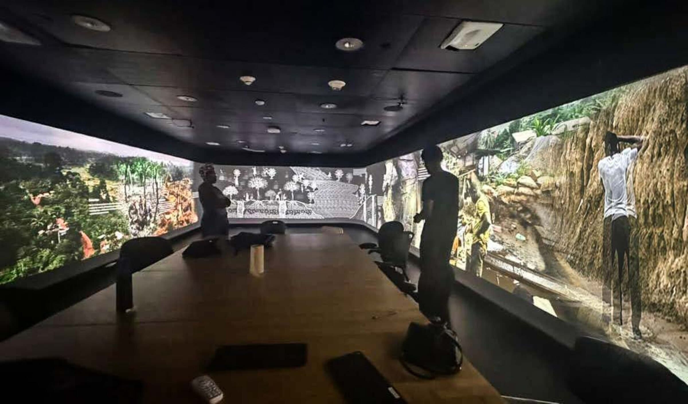 Photograph of an immersive exhibition room at the Yale School of Architecture, a wraparound photographic mural of a mining landscape with visitors examining it.