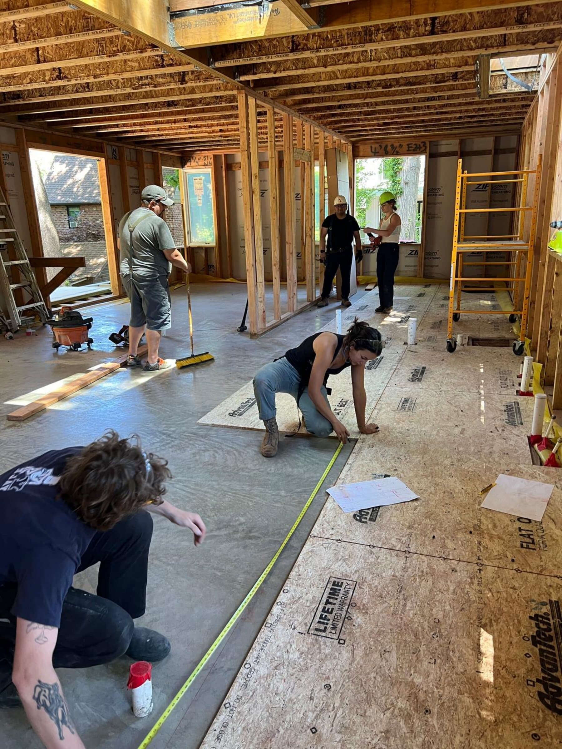 Construction photograph of team members measuring and installing the floor finish inside the framed house.
