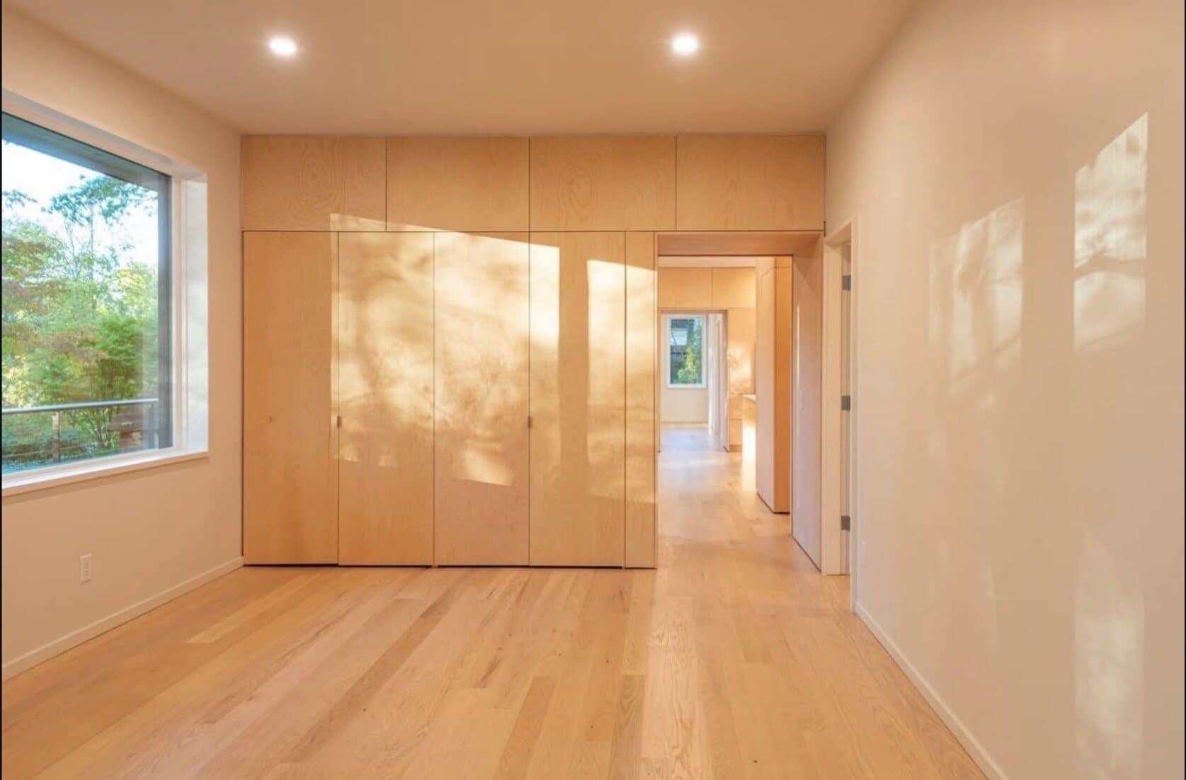 Photograph of the finished house's hallway, light wood flooring and built-in cabinetry leading toward a sunlit window.